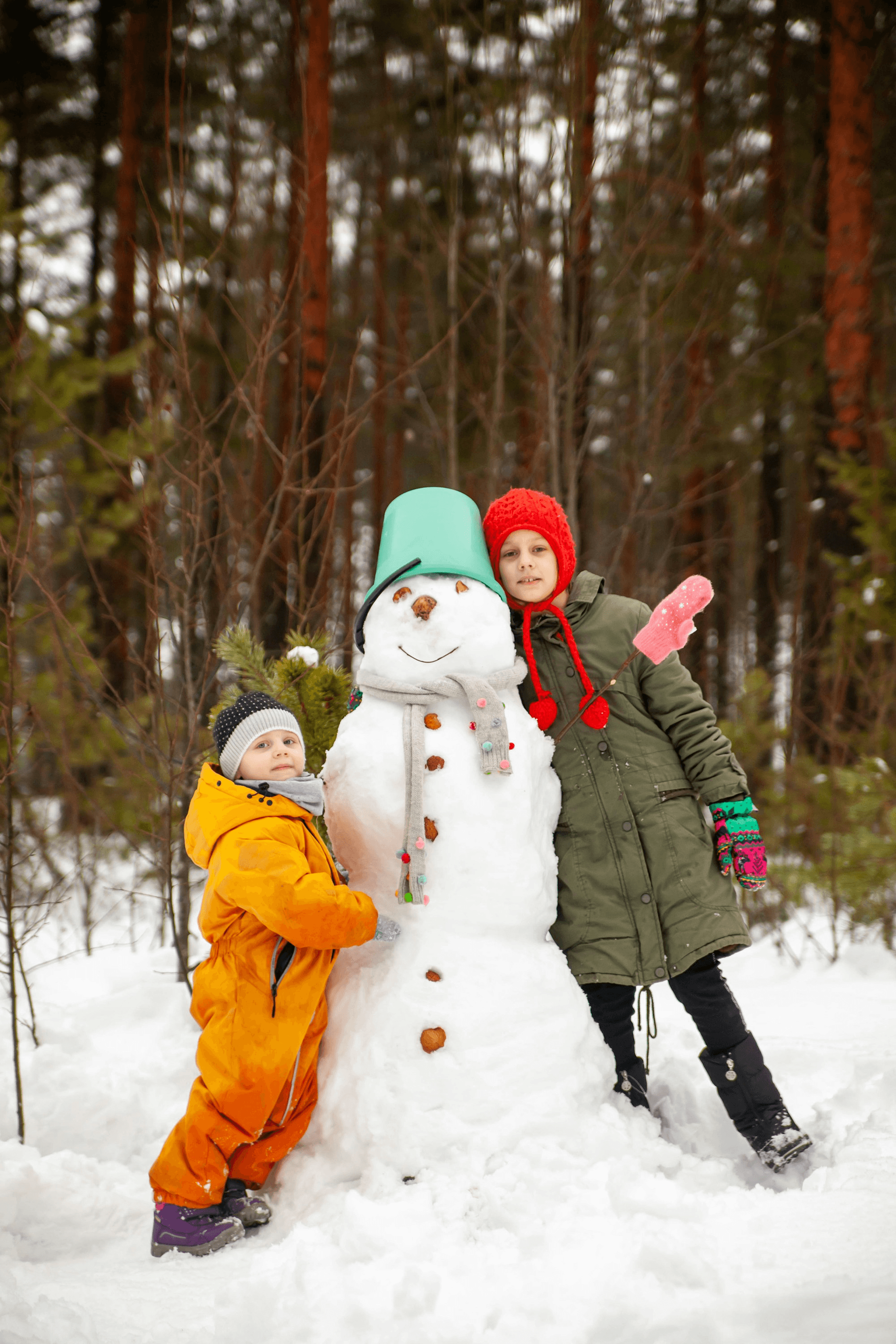 Two children proudly standing with their snowman in a Finnish forest.