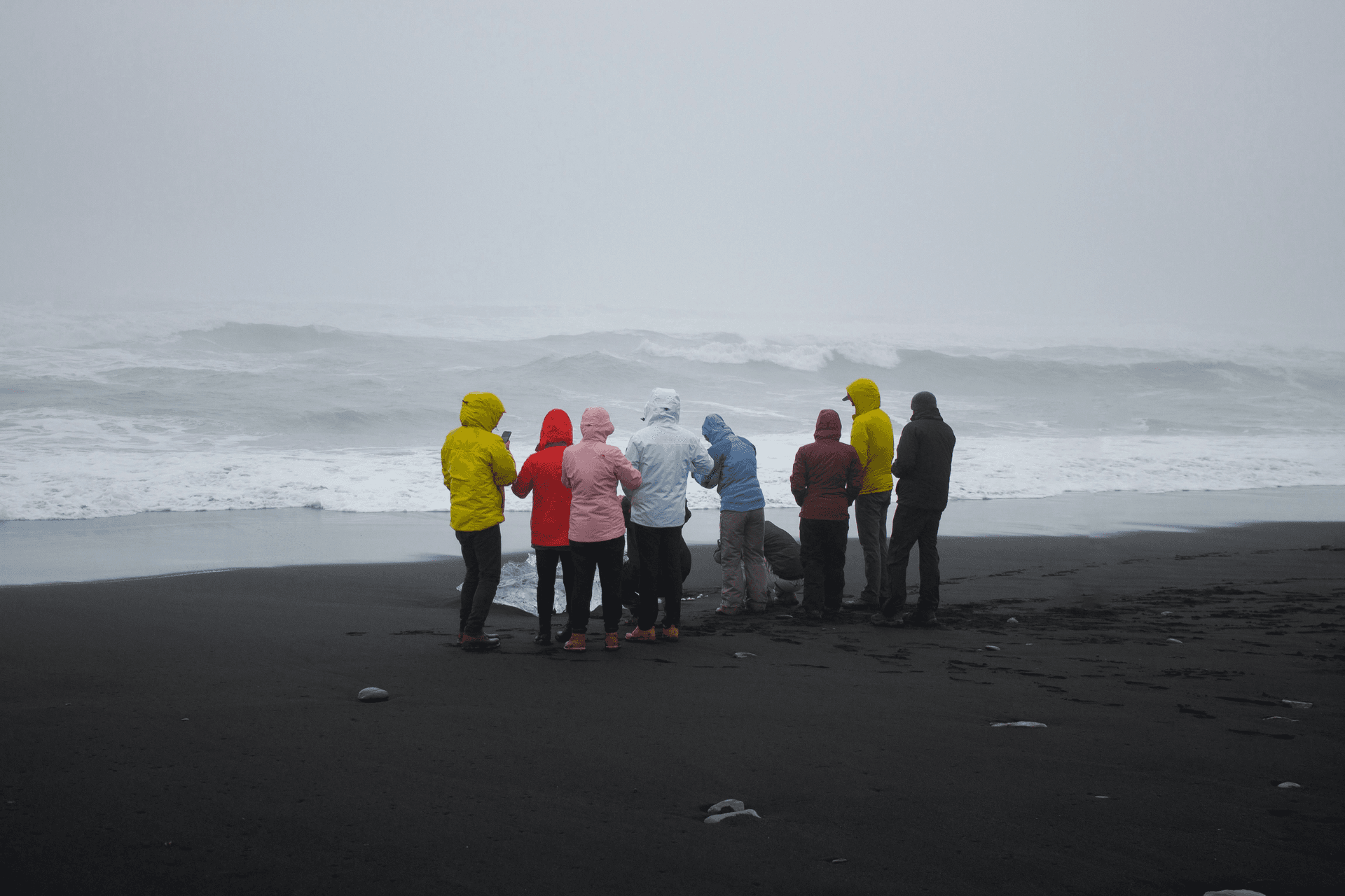 Bright jackets on a family group standing on Iceland’s black-sand beach in moody sea mist.